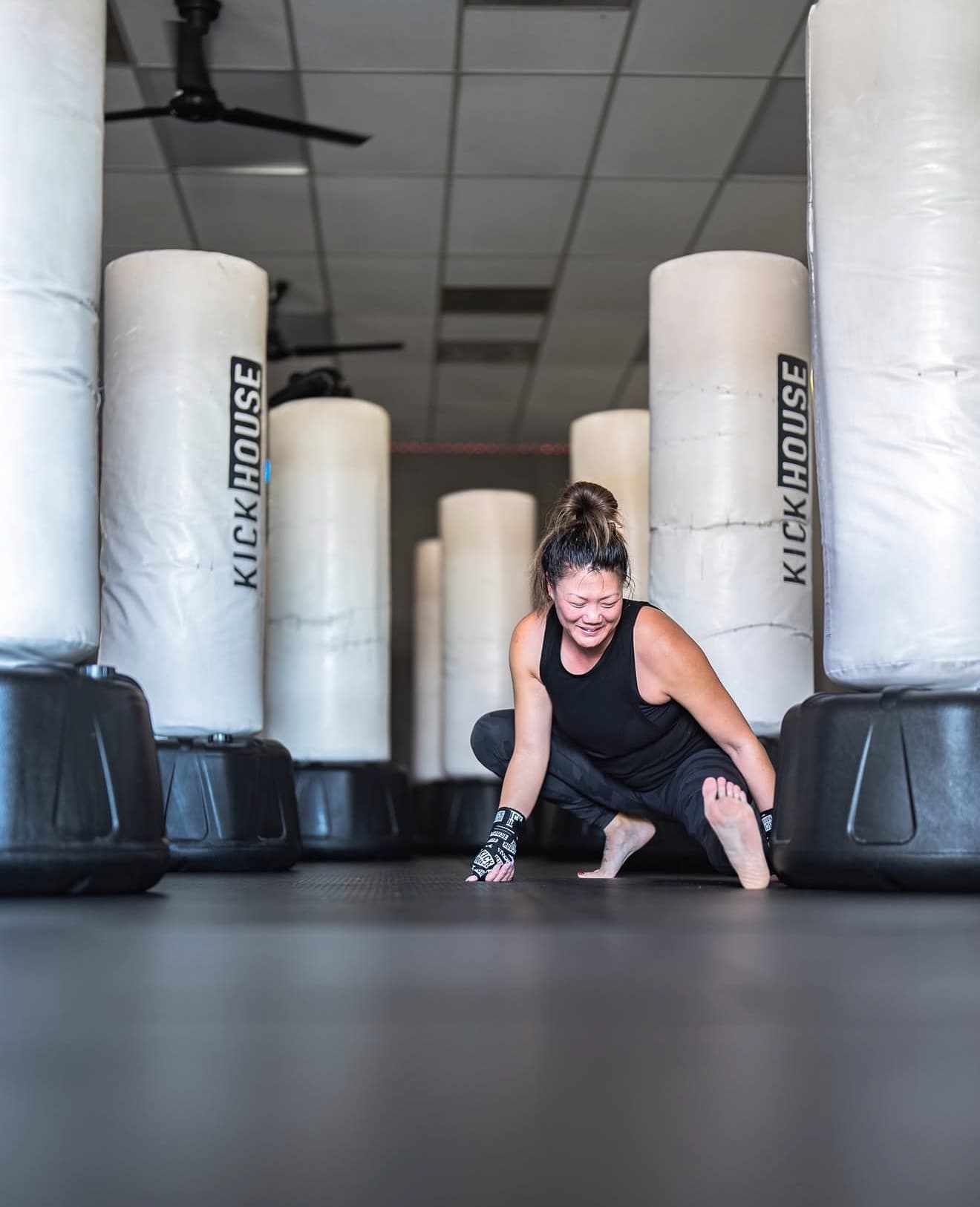 A KickHouse member stretching on the mat between rows of free-standing heavy bags